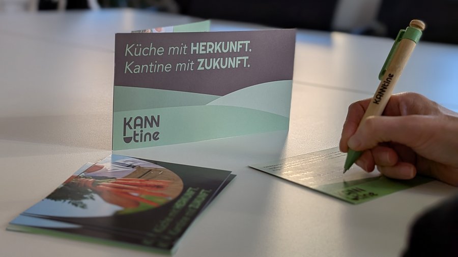 3 Flyer auf einem Tisch, eine Hand mit Stift, die einen Flyer ausfüllt