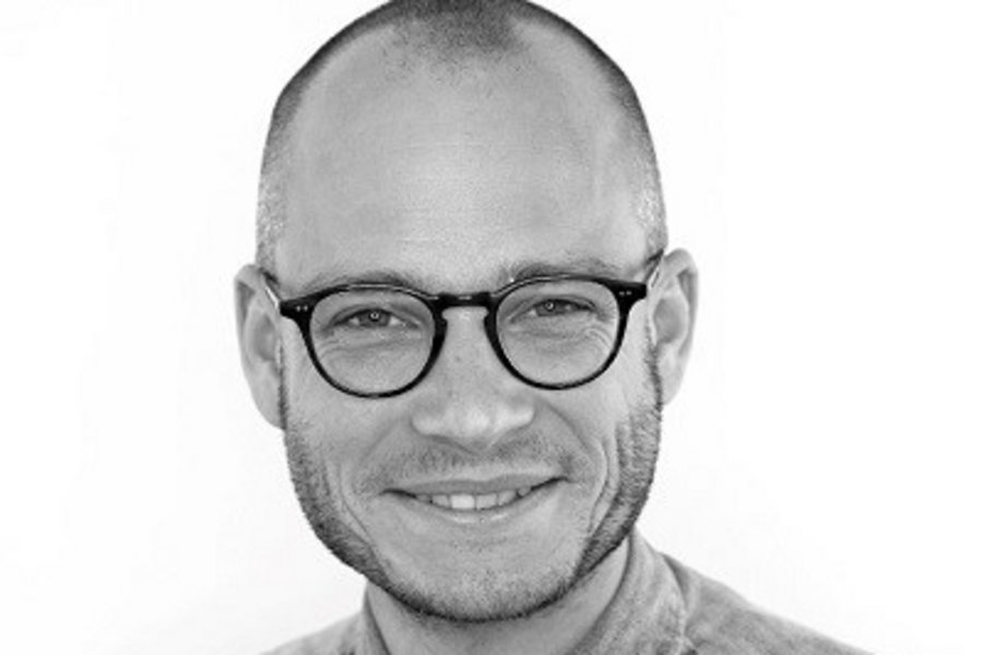 Schwarz-weiß Bild - ein Mann mit kurz geschorenen Haaren und Brille lächelt