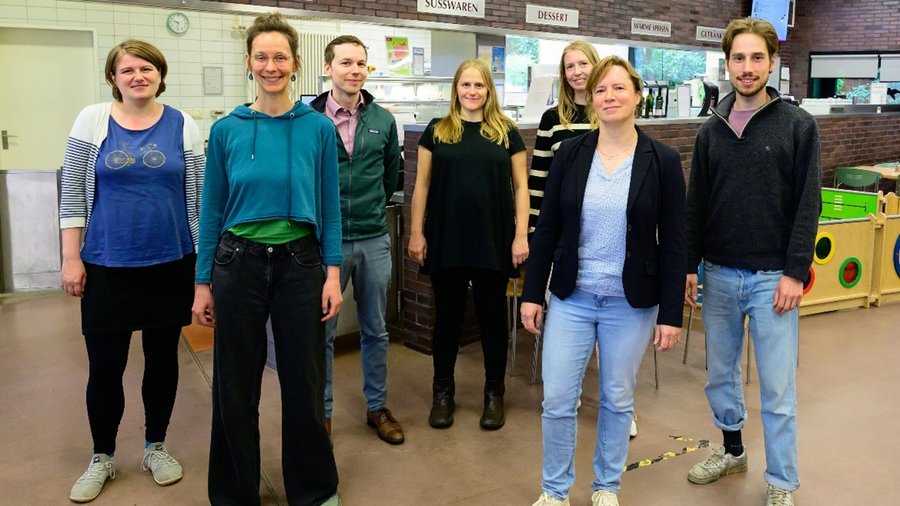 7 Personen stehen in einer Kantine